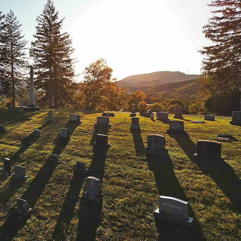 Cemetery at sunrise with headstones in foreground and mountains in background.